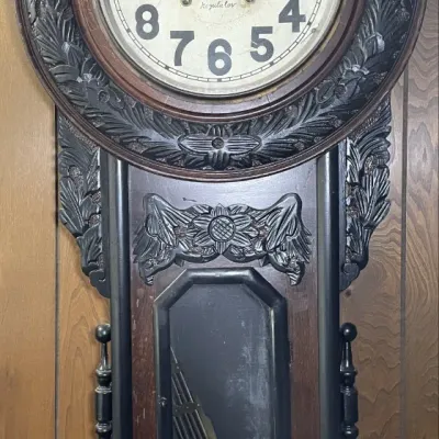 Sale Photo Thumbnail #67: Antique Regulator wall clock featuring an intricately carved dark wood case, floral accents, and a lower glass display window showing the pendulum.