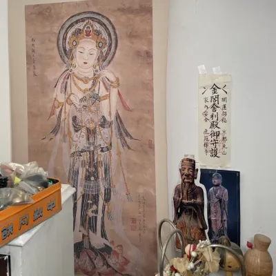 Sale Photo Thumbnail #65: Large Japanese hanging scroll painting depicting the Bodhisattva Guanyin (Kannon), framed by calligraphy talismans, wooden kokeshi dolls, and traditional art prints.