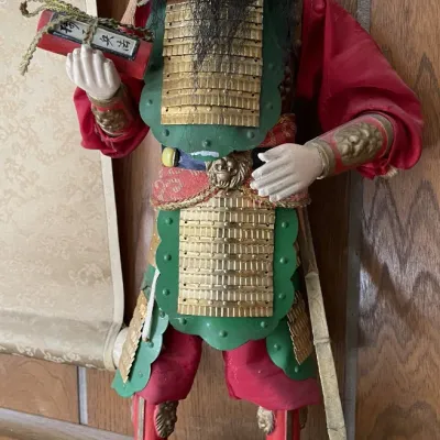 Sale Photo Thumbnail #20: Vintage Japanese warrior doll (Musha ningyo) depicting a samurai in full armor with a beard, holding a scroll, mounted on a carved wooden base.
