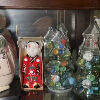 Sale Photo Thumbnail #183: Collection of Asian dolls and glass items, including Hakata figurines, a boxed traditional doll, and clear glass Christmas tree-shaped containers filled with colorful glass marbles.