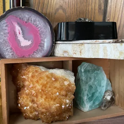 Sale Photo Thumbnail #77: Collection of mineral specimens and geode slices, including a polished pink dyed agate slab, a large citrine cluster, and raw fluorite displayed on wooden shelving.