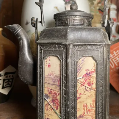 Sale Photo Thumbnail #134: Antique Chinese pewter hexagonal teapot featuring inset decorated panels with narrative scenes, a fixed overhead handle, and geometric border details.