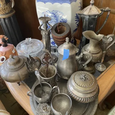 Sale Photo Thumbnail #78: Collection of vintage silver-plate and metal decorative items, including teapots, pitchers, serving pieces, and a figural caryatid candlestick.