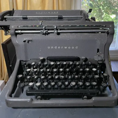 Sale Photo Thumbnail #49: Vintage Underwood manual typewriter with a dark gray crinkle finish and round black keycaps, showing dust and signs of age.