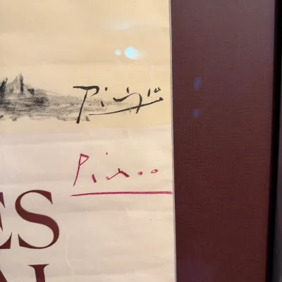 Sale Photo Thumbnail #213: Close-up detail of a framed vintage exhibition poster featuring Pablo Picasso's printed and handwritten signatures on aged paper.