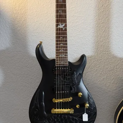 Sale Photo Thumbnail #90: Custom matte black electric guitar featuring carved eagle and feather motifs, gold hardware, and Asian character fretboard inlays.
