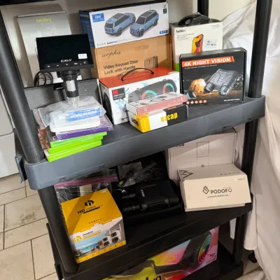 Sale Photo Thumbnail #292: boxed consumer electronics, small gadgets, security cameras, and a Jetson Lumino hoverboard.