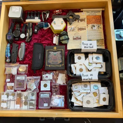 Sale Photo Thumbnail #61: Wooden display case featuring a collection of collectibles, including flip-card coins, pocket knives, wristwatches, gemstones, and historical currency.