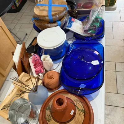 Sale Photo Thumbnail #262: Selection of kitchenware and home goods including blue cobalt glass baking dishes, a terracotta tagine, a flour sifter, air fryer paper liners, and various small utensils.