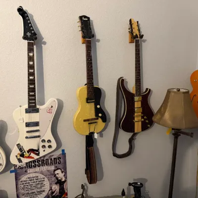 Sale Photo Thumbnail #89: Collection of vintage electric guitars, including a white Firebird style, a Supro, and an Epiphone hollow body, displayed alongside a Crossroads Guitar Festival poster.