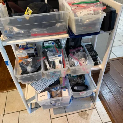 Sale Photo Thumbnail #290: White plastic shelving unit filled with clear storage bins containing miscellaneous electronics, cables, computer accessories, and small items.