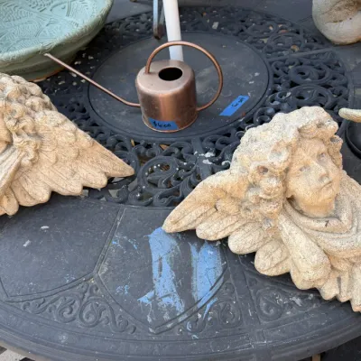 Sale Photo Thumbnail #385: Pair of cast stone cherub wall sconces sitting on a wrought-iron patio table alongside a small copper watering can.