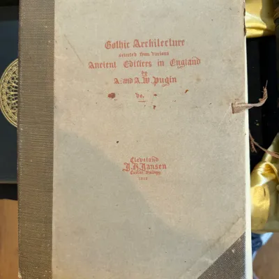 Sale Photo Thumbnail #69: Antique volume of "Gothic Architecture selected from various Ancient Edifices in England" by A. and A.W. Pugin, published by J.H. Jansen in Cleveland, 1919. Features a quarter-cloth binding with light wear and foxing on the cover.