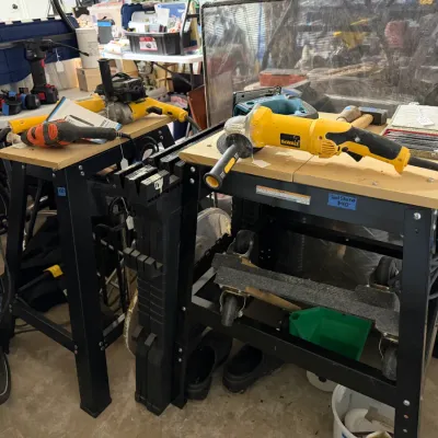Sale Photo Thumbnail #327: Pair of black metal tool stands with wooden tops, featuring various power tools including a DeWalt angle grinder and reciprocating saws.