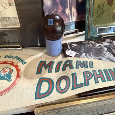 Sale Photo Thumbnail #47: Collection of Miami Dolphins sports memorabilia, featuring a vintage felt pennant, autographed framed photos including Dan Marino, and a vintage leather baseball.