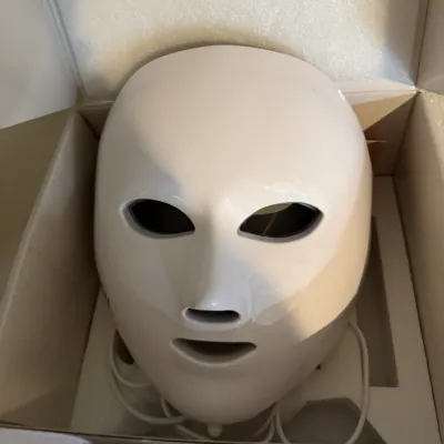 Sale Photo Thumbnail #293: White LED facial light therapy mask with power cord, resting in its original packaging.
