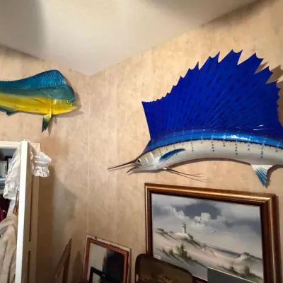 Sale Photo Thumbnail #248: Two taxidermy or fiberglass fish wall mounts, featuring a vibrant blue sailfish and a yellow and blue mahi-mahi, displayed above framed artwork.