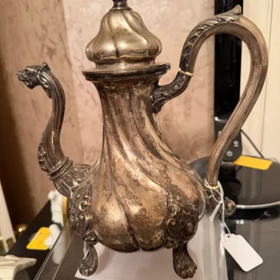 Sale Photo Thumbnail #280: Vintage silver-plated teapot featuring a swirling fluted body, ornate animal-head spout, decorative finial lid, and carved scroll handle.