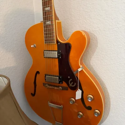 Sale Photo Thumbnail #97: Epiphone hollow-body electric guitar in a natural blonde finish, featuring twin pickups, f-holes, and a signature logo pickguard.