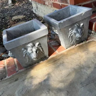 Sale Photo Thumbnail #283: Pair of square concrete planters featuring relief lion head motifs on each side, painted silver.