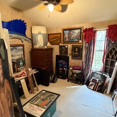 Sale Photo Thumbnail #245: An eclectic collection of artwork and decor in a room, featuring framed paintings, prints, a mounted blue sailfish, and wooden furniture.