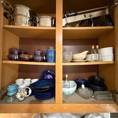 Sale Photo Thumbnail #259: Wooden kitchen cabinet filled with assorted cookware, blue stoneware dishware, purple mini cocottes, glass containers, and kitchen gadgets.