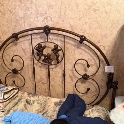 Sale Photo Thumbnail #276: Ornate dark metal full-size bed featuring scrollwork detail and a central medallion with cherub figures.