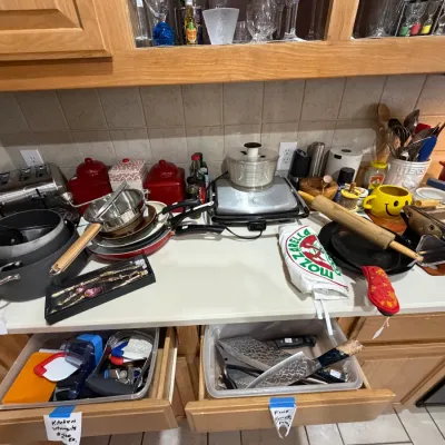 Sale Photo Thumbnail #255: Assorted kitchenware including pots, pans, a food processor, pasta maker, rolling pin, and chef knives.