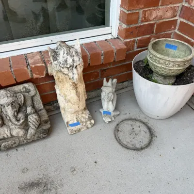 Sale Photo Thumbnail #391: Collection of concrete and stone outdoor decor, including a Ganesha wall relief, gargoyle statues, and a small urn placed inside a larger planter.