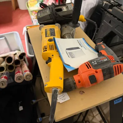 Sale Photo Thumbnail #325: Collection of power tools including a yellow DeWalt reciprocating saw, an orange corded drill, and a heavy-duty angle grinder with side handle on a worktable.