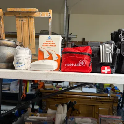 Sale Photo Thumbnail #362: Assortment of emergency and medical supplies, including a red first aid pouch, tactical bags, a disposable skin stapler box, and a brass pot.