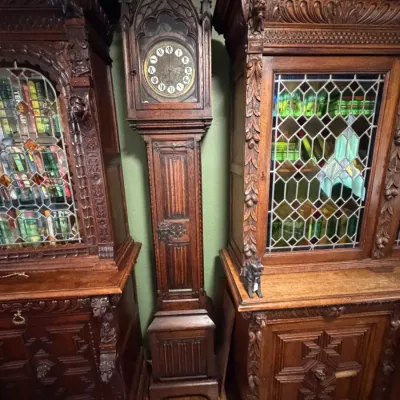 Sale Photo Thumbnail #7: Antique Gothic Revival carved oak tall case clock positioned between two matching leaded-glass cabinets.