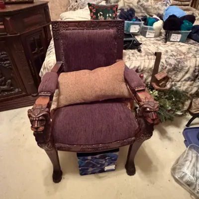 Sale Photo Thumbnail #273: Ornately carved wooden armchair featuring carved lion head armrests and claw feet, upholstered in purple fabric with nailhead trim.