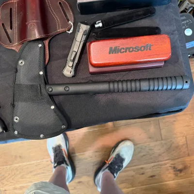 Sale Photo Thumbnail #52: Collection of outdoor and specialty gear including a black tactical hatchet with sheath, leather holsters, pocket knife, and a Microsoft-branded wooden pen box.