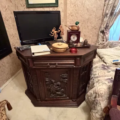 Sale Photo Thumbnail #274: Ornately carved dark wood hexagonal cabinet with a central panel depicting a equestrian scene, topped with a flat-screen TV and various decorative accents.