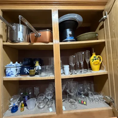 Sale Photo Thumbnail #256: Wooden cabinet shelves filled with kitchenware and glassware, including cookware, mugs, stemware, and decorative oil dispensers.