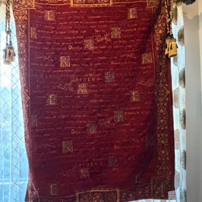 Sale Photo Thumbnail #187: Deep red and gold tapestry featuring printed Latin text and ornate floral borders, suspended on a hanging rod with decorative side tassels.