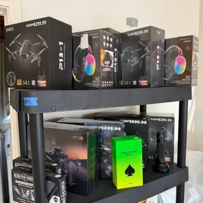 Sale Photo Thumbnail #291: Black plastic utility shelving unit holding boxed electronics, including fold-out drones, RGB active noise-canceling headphones, solar power banks, and night vision devices.