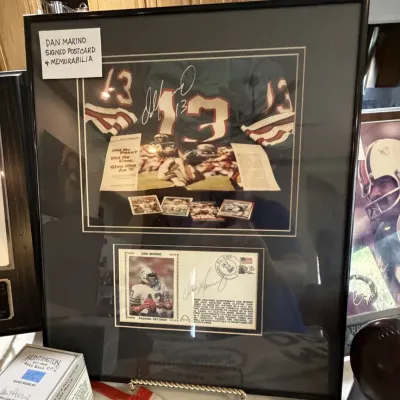 Sale Photo Thumbnail #46: Framed Dan Marino autographed sports memorabilia display featuring a signed first day cover postcard, trading cards, and jersey graphic in a black frame.