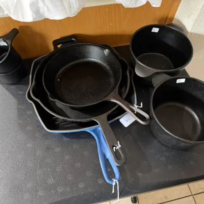 Sale Photo Thumbnail #266: Collection of black cast iron cookware including skillets, deep pots, and a blue enamel-coated grill pan.