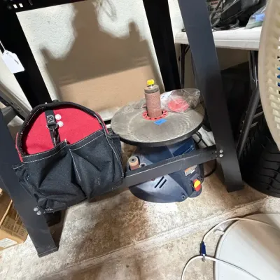 Sale Photo Thumbnail #303: Ryobi benchtop oscillating spindle sander stored beneath a metal workbench alongside a black and red canvas tool bag.