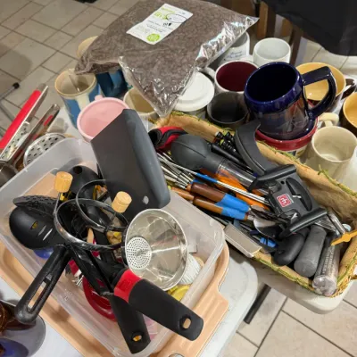 Sale Photo Thumbnail #263: Collection of assorted kitchen utensils, ceramic coffee mugs, and a bag of whole-bean coffee resting on a folding table.