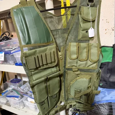 Sale Photo Thumbnail #334: Olive green mesh tactical vest featuring multiple utility pouches, shell loops, and a cross-draw holster on a plastic hanger.