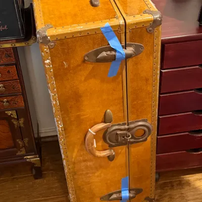 Sale Photo Thumbnail #123: Vintage early-to-mid 20th century standing wardrobe trunk in yellow tweed finish, featuring metal corner guards, brass latches, and a leather side handle.