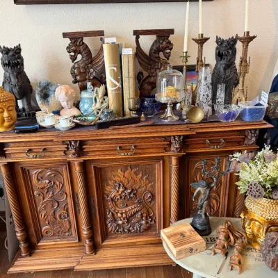 Sale Photo Thumbnail #130: Ornately carved antique wooden sideboard featuring dragon relief paneling, topped with eclectic home decor including Foo dog statues, brass candlesticks, and a Buddha head bust.