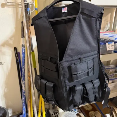 Sale Photo Thumbnail #336: Black tactical vest with multiple pockets and webbed straps hanging on a plastic hanger, made in the USA.