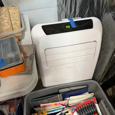 Sale Photo Thumbnail #353: SereneLife white portable air conditioner powered next to a bin of office supplies and notebooks.